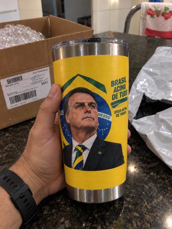 Copo térmico amarelo com estampa Brasil acima de tudo, segurado na mão